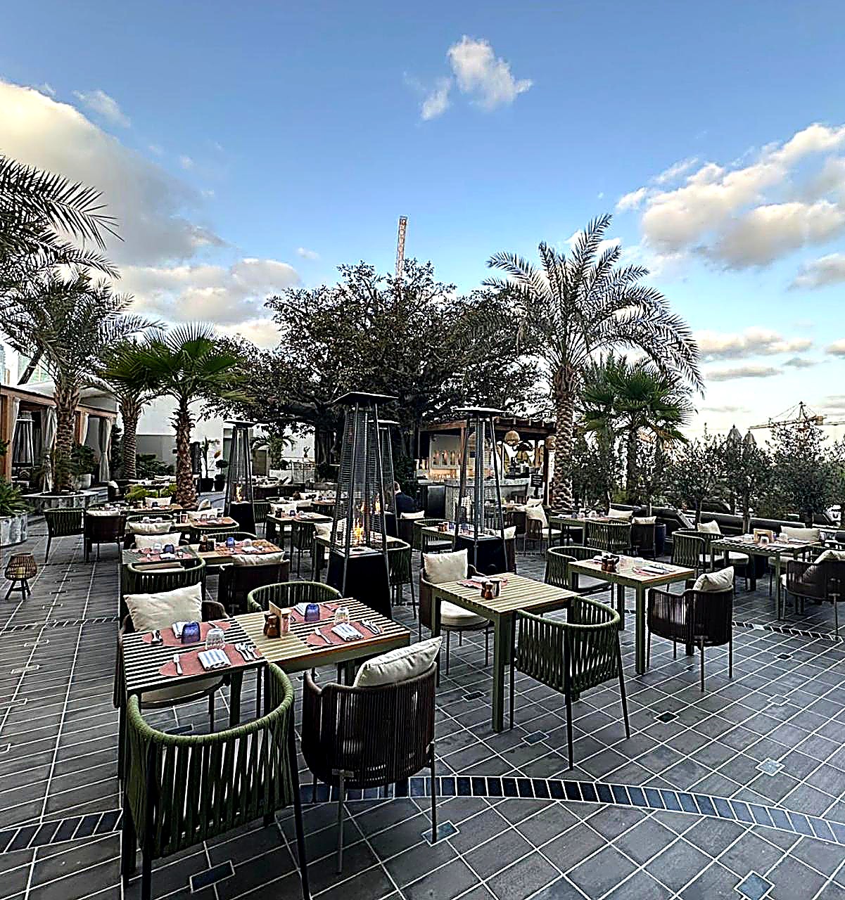 Rooftop restaurant terrace at dusk with rope dining chairs and palms, outdoor hospitality furniture Dubai