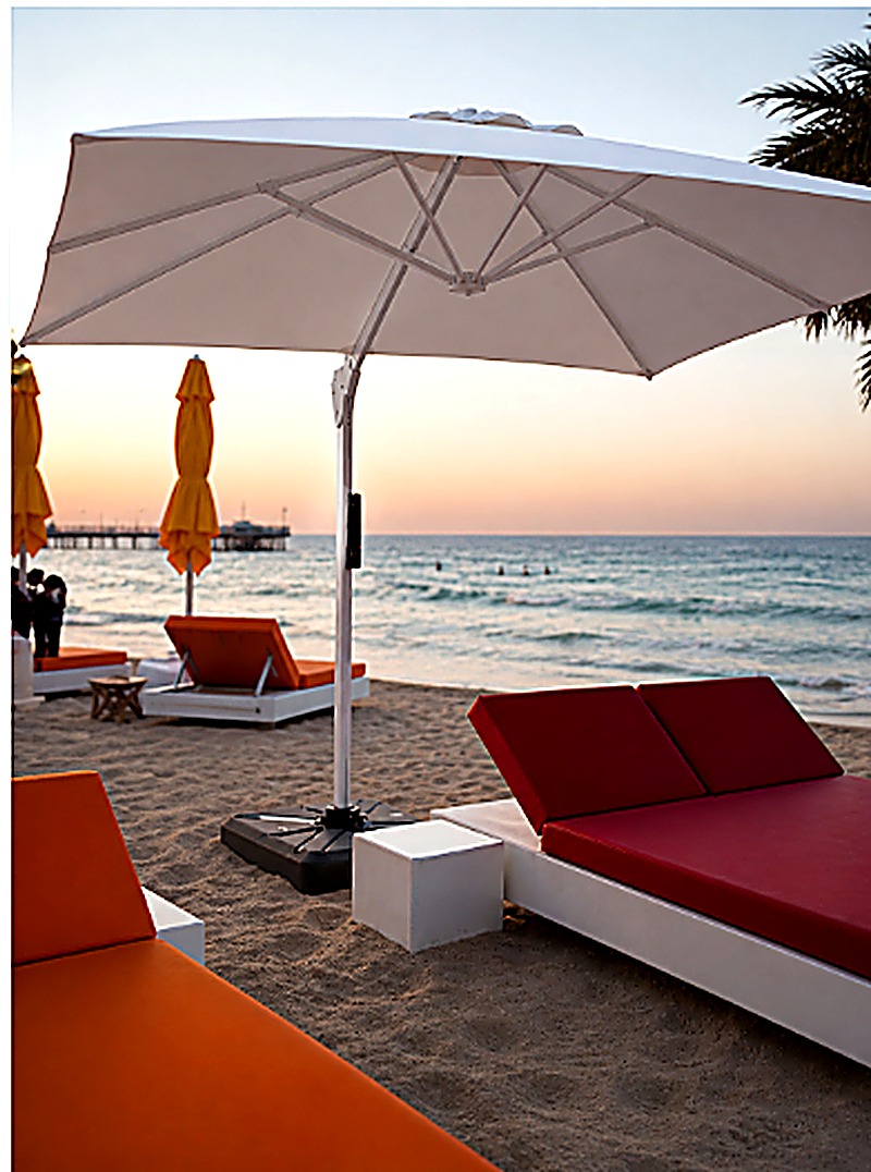 White cantilever umbrella and daybed on a hotel beach at sunset