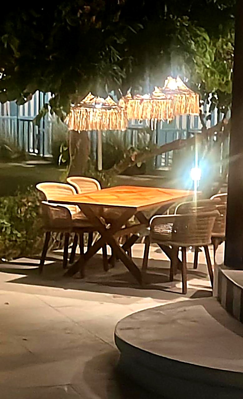 Evening garden dining with raffia umbrellas and teak table, hotel outdoor furniture