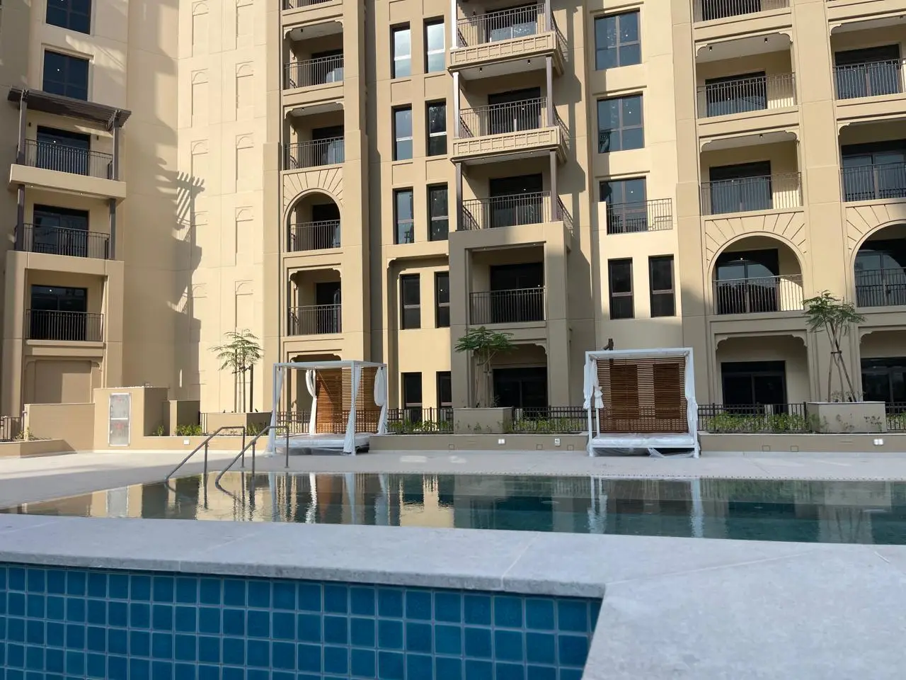 Custom pool deck cabanas with matte white powder-coated frames and Grade A teak slatted back panels installed beside the pool at a five-star hospitality development in Dubai